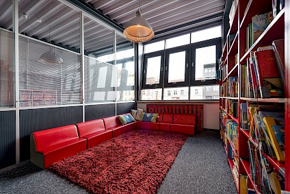 The Picasso group reading room of with a red corner sofa, teddy carpet and a whole wall full of books